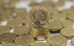 pound coins are scattered around with a tower of coins standing in the middle
