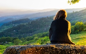 a woman sits gazing out into the countryside, basking in hazy sunshine